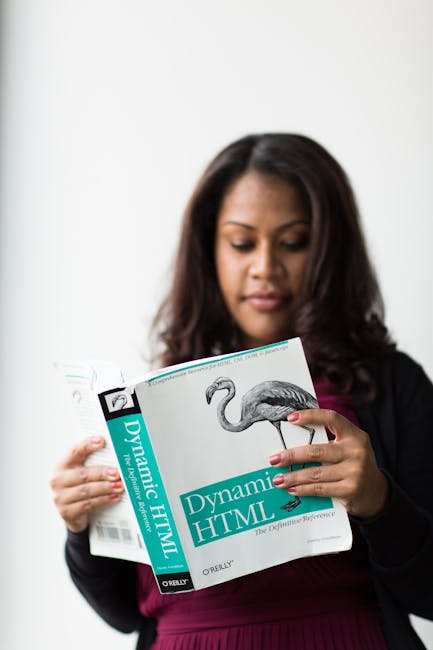 A woman with medium skin tone and dark, wavy hair is holding a thick book titled 'Dynamic HTML' published by O'Reilly, which features a detailed illustration of a flamingo on the cover. She is standin