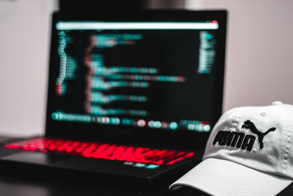 A close-up photograph of a laptop computer displaying lines of programming code on its screen, with a beige ceramic coffee mug placed to the right of the laptop. The mug features printed text that rea